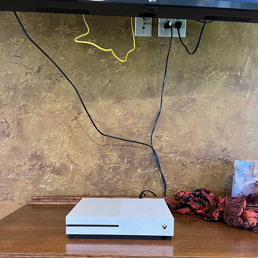 A wall mounted TV with cables and wires dangling down the wall to a cable box.